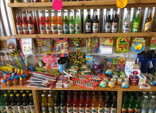 A colorful display of candies, sodas, and toys arranged on wooden shelves in a shop.