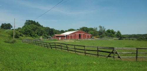 A red barn surrounded by green fields and a wooden fence under a clear blue sky.