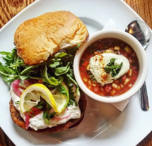 A sandwich with arugula, lemon, and creamy filling, served with a bowl of soup topped with herbs and a dollop of cream.
