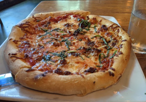 A freshly baked pizza with melted cheese, tomato sauce, and basil on a wooden table next to a glass of water.
