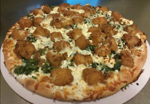 A pizza topped with creamy white sauce, spinach, and golden-brown chicken pieces on a thick crust.