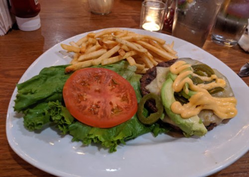A plate with a burger topped with lettuce, tomato, jalapeños, and sauce, served with a side of French fries.
