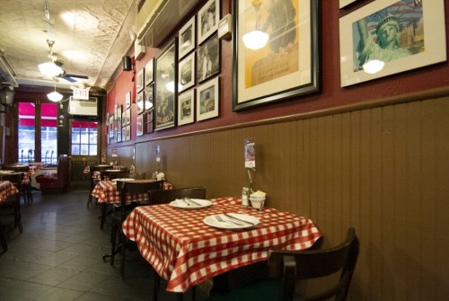 Cozy restaurant interior with checkered tablecloths, framed photos on the walls, and warm lighting.