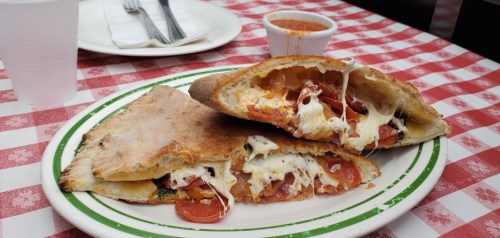A plate of cheesy calzones filled with pepperoni, served with marinara sauce on a checkered tablecloth.