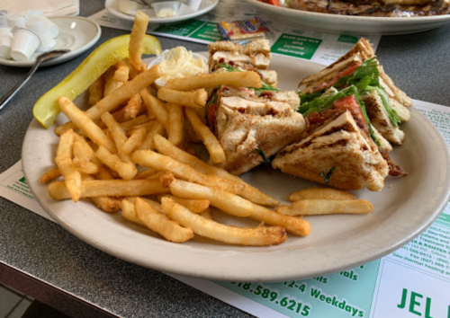 A plate with a club sandwich, lettuce, tomato, and fries, accompanied by a pickle and a small dish of butter.