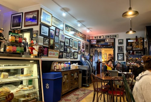 Cozy café interior with framed photos, a display case of pastries, and patrons enjoying their drinks.