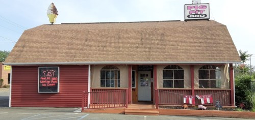 A red and tan building with a sign for "Pig Pit BBQ" and an ice cream cone on the roof. Outdoor seating area visible.