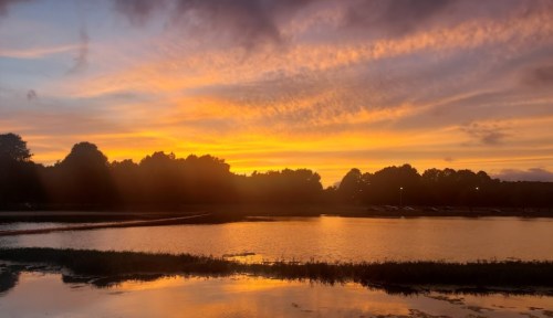 A vibrant sunset over a calm lake, with colorful clouds reflecting on the water's surface.