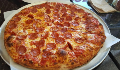 A large pepperoni pizza on a silver tray, with melted cheese and a golden-brown crust.