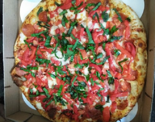 A pizza topped with pepperoni, fresh tomatoes, and basil, in a cardboard box.