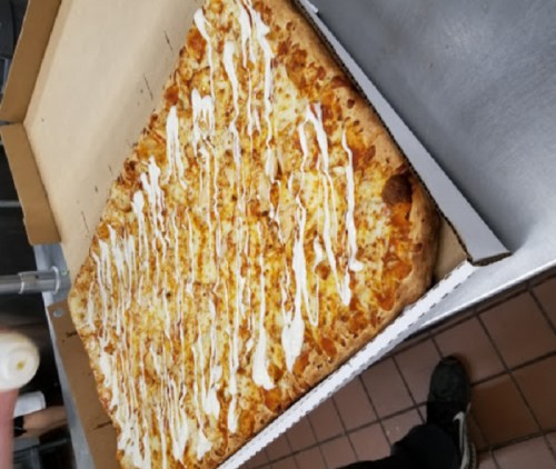 A large rectangular pizza topped with drizzled sauce, placed in an open pizza box on a countertop.