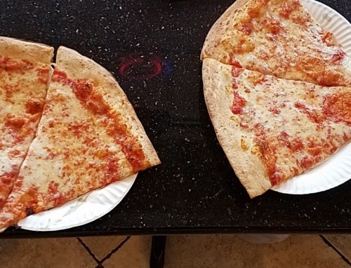 Two slices of cheese pizza on white paper plates, placed on a black table.