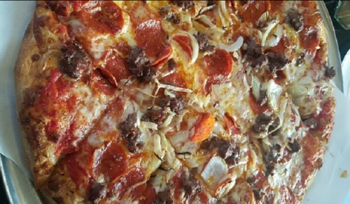 A close-up of a pizza topped with pepperoni, sausage, onions, and melted cheese on a golden crust.