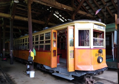 A vintage streetcar, numbered 5645, inside a rustic train shed with wooden beams and an American flag.