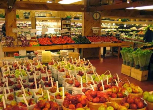 A vibrant grocery store display filled with baskets of apples, colorful fruits, and fresh vegetables on wooden shelves.