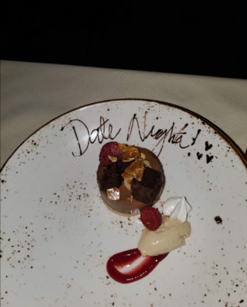 A dessert plate with a chocolate mousse, raspberries, cream, and "Date Night!" written in chocolate sauce.