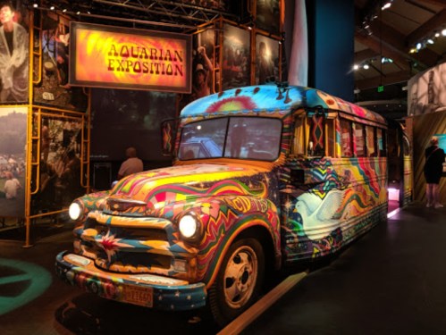 A colorful, psychedelic bus on display at an exhibition, surrounded by vibrant artwork and lighting.