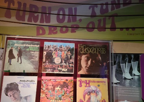 Display of iconic album covers, including The Beatles and Jimi Hendrix, with a colorful "Turn on, tune in, drop out" sign.