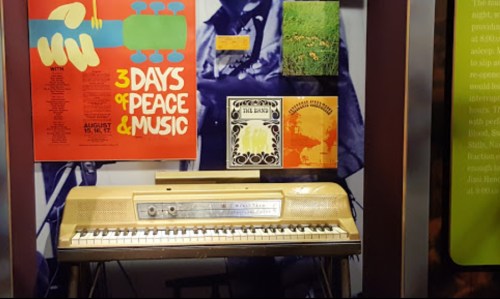 A vintage keyboard displayed with posters and album covers from the 1969 Woodstock festival.