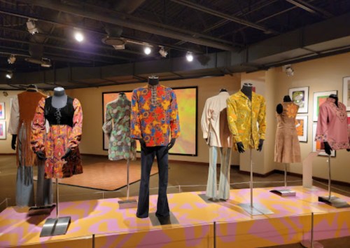 A display of colorful vintage clothing on mannequins in an art gallery setting.