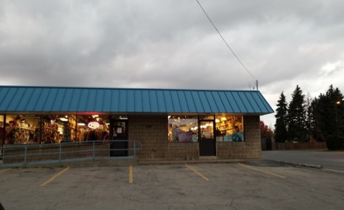 A storefront with a blue roof, large windows displaying merchandise, and a cloudy sky overhead.