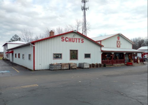 A white and red building with "Schutt's" signage, featuring a porch and surrounded by trees under a cloudy sky.