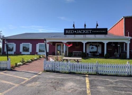 A pink farm store with a sign reading "Red Jacket Farmstore," surrounded by greenery and a white picket fence.