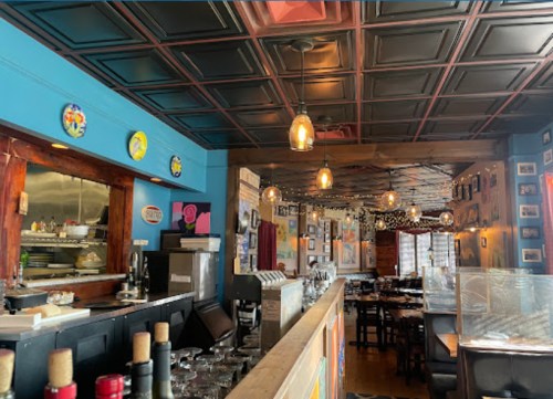 A colorful restaurant interior with a bar, decorative plates on the walls, and warm lighting.