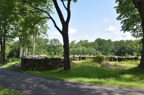 A scenic view of a stone wall surrounded by trees and greenery, with a pathway in the foreground.