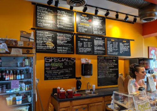 A colorful café menu on a wall with various food options, and a barista serving customers at the counter.