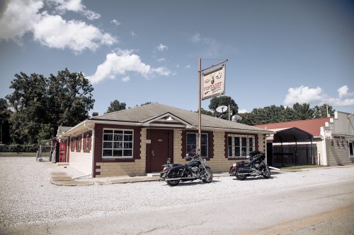 A vintage building with a sign, flanked by two parked motorcycles, under a clear blue sky.