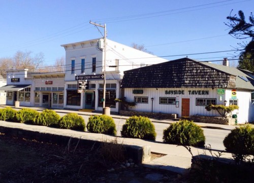 A quaint street scene featuring a market and Bayside Tavern, surrounded by greenery and clear blue skies.