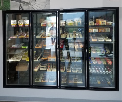 A glass-fronted refrigerator displaying various packaged food items and snacks on shelves.