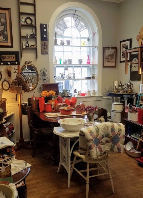 Cozy vintage shop interior with a wooden table, colorful decor, and various antiques displayed on shelves and walls.
