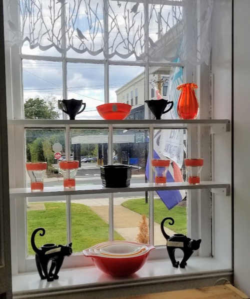 A window display featuring colorful glassware and decorative cat figurines against a street view.