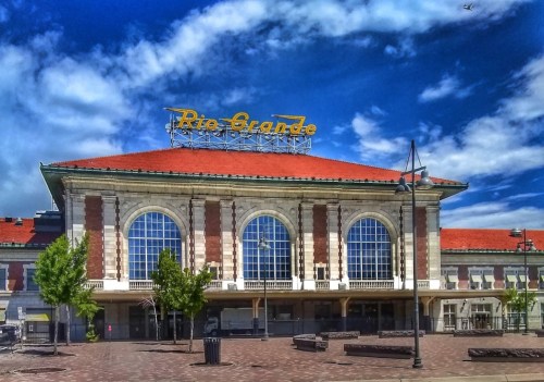 Historic building with a red-tiled roof and large arched windows, featuring a "Rio Grande" sign against a blue sky.