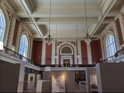Interior of a spacious gallery with high ceilings, large windows, and modern art displays in the foreground.
