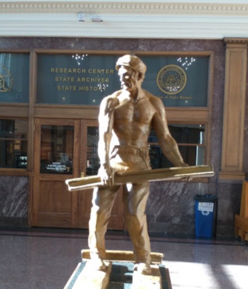 A bronze statue of a muscular worker holding a beam, set in a historic building's entrance.