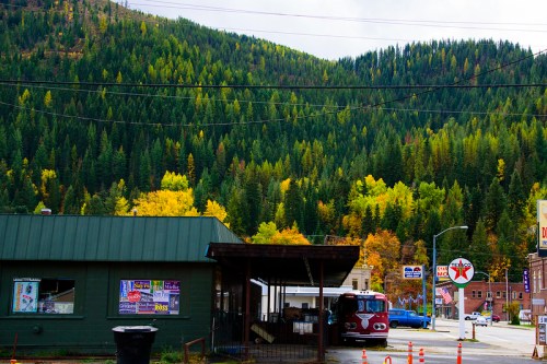 A small green building with a covered area, surrounded by vibrant autumn trees and a mountainous backdrop.