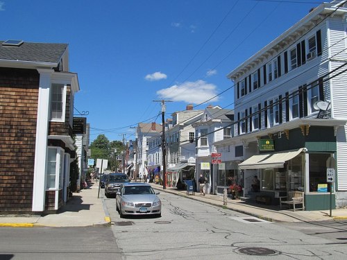 A quaint street scene featuring shops, parked cars, and blue skies in a small town.