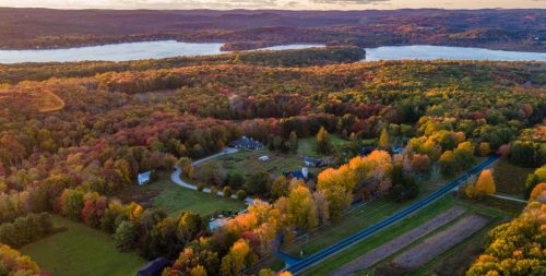 Aerial view of a colorful autumn landscape with trees, a lake, and winding roads under a sunset sky.