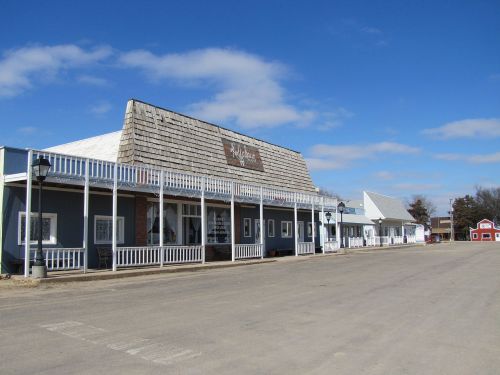A quiet, empty street lined with old-style buildings under a blue sky with scattered clouds.