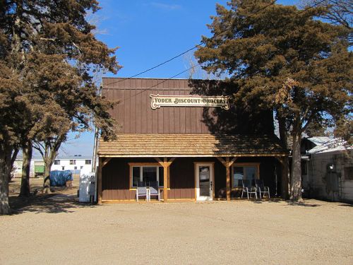 A rustic wooden store with a sign reading "Yoder Discount Grocer," surrounded by trees and gravel.