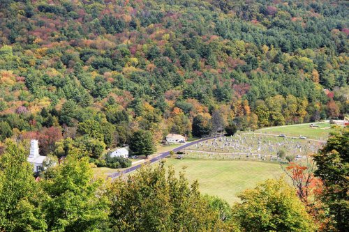 Aerial view of a cemetery surrounded by vibrant autumn foliage and rolling hills.