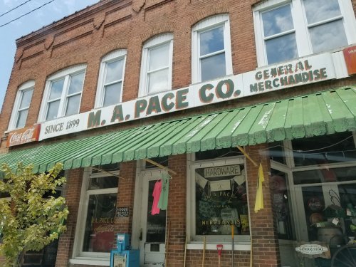 A brick storefront with a green awning, displaying "M.A. Pace Co. General Merchandise" and "Since 1899."