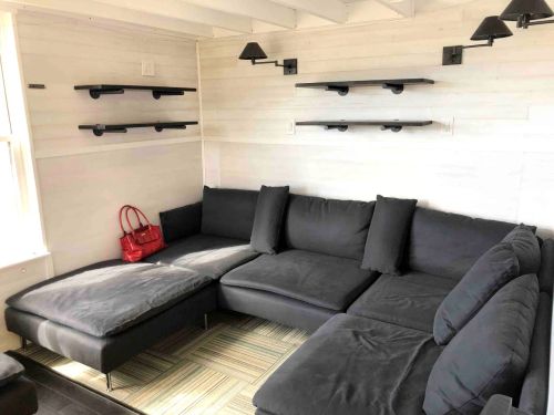 Cozy living room with a dark sectional sofa, wall-mounted shelves, and a red handbag on the floor.