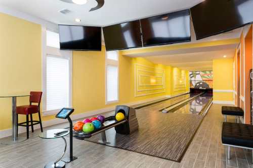 A modern bowling alley with colorful bowling balls, sleek lanes, and large screens in a bright yellow room.
