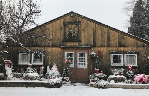 A cozy wooden cabin decorated for the holidays, surrounded by snow and festive plants.
