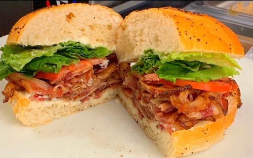 A freshly cut sandwich with layers of bacon, lettuce, and tomato, served on a toasted bun.
