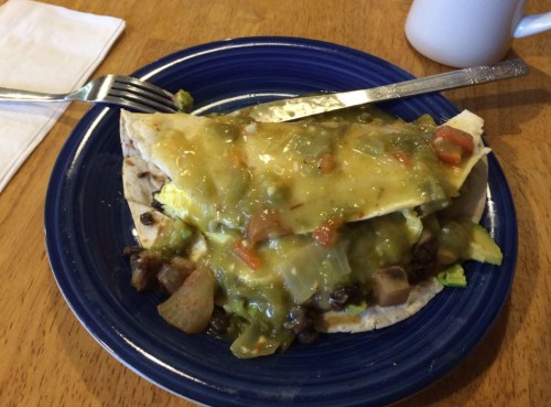A plate with a tortilla topped with green sauce, black beans, and diced vegetables, served with a fork.